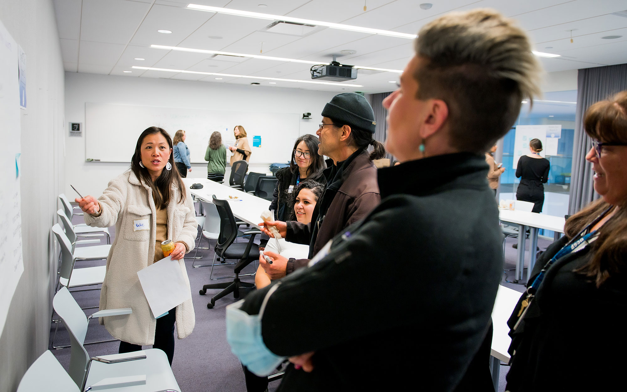 Woman gestures toward white board as people gather and listen