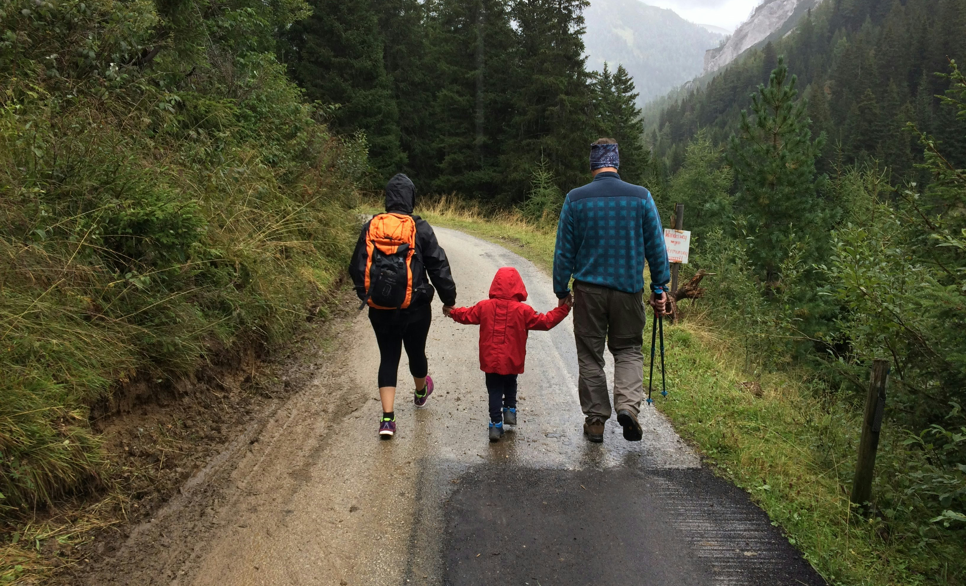 Parents hold kid's hands while on rainy hike