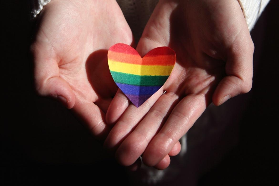 Hand holding paper heart with pride rainbow flag colors