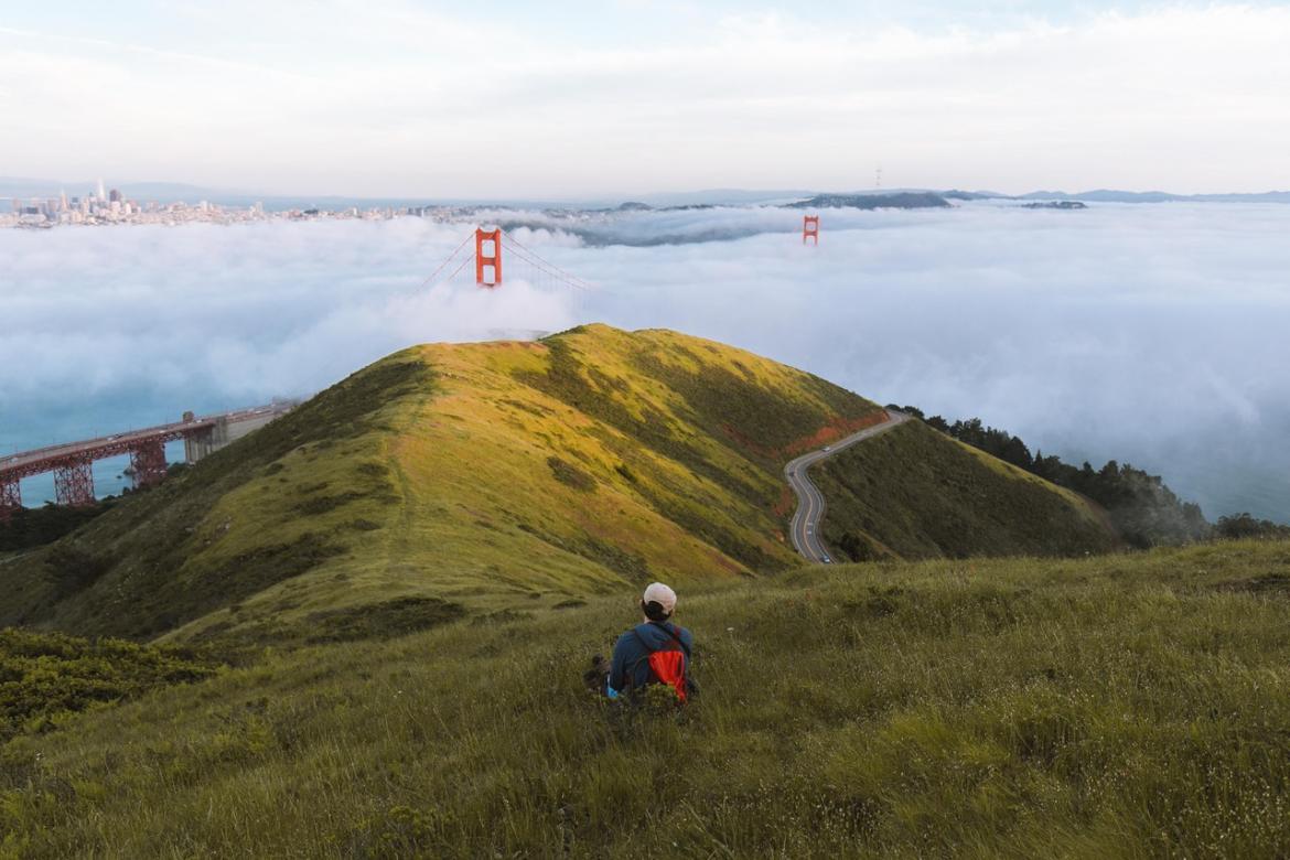 Person on green hillside staring at Golden Gate Bridge