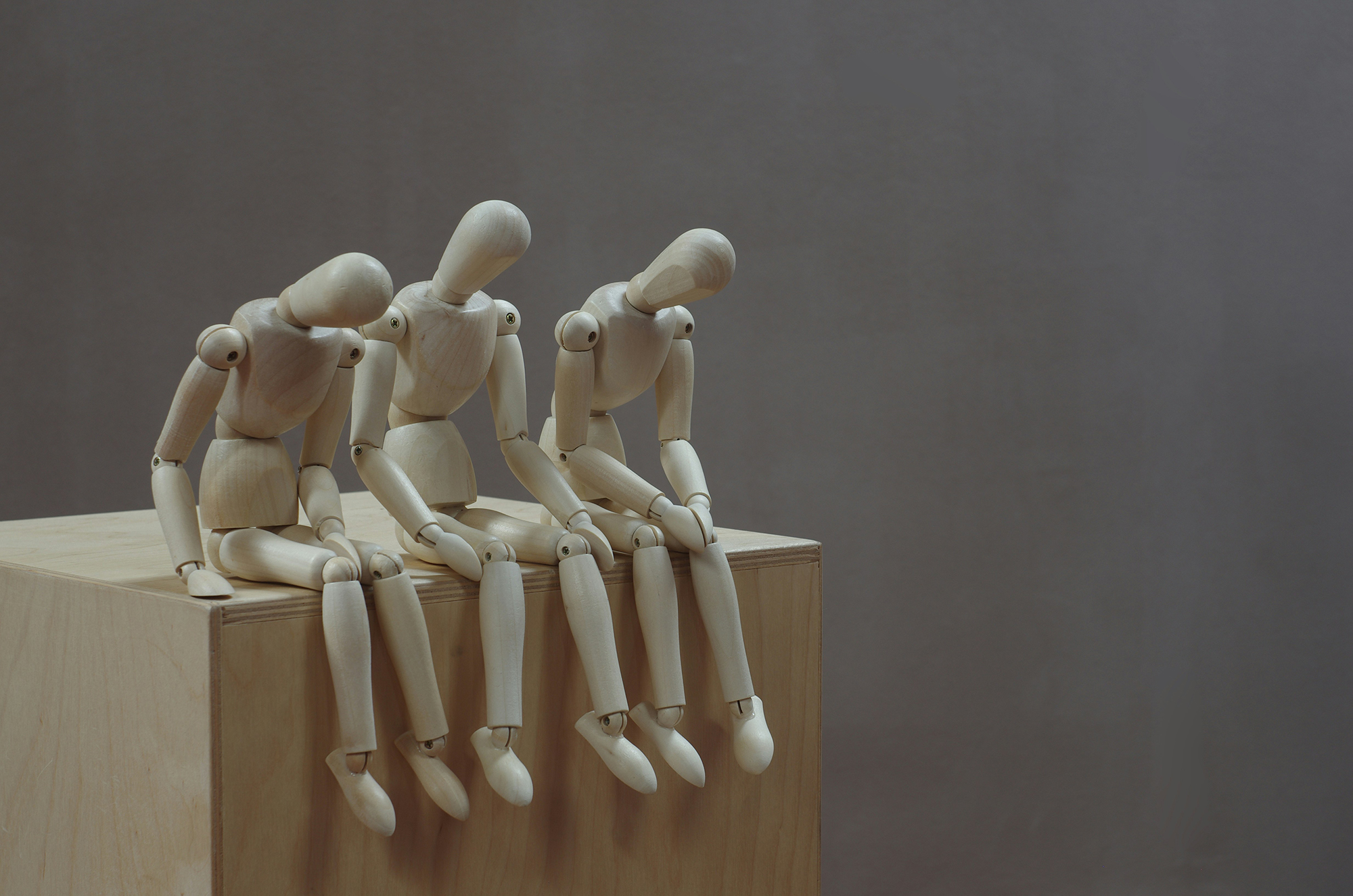 Three wooden figurines sitting down and looking sad