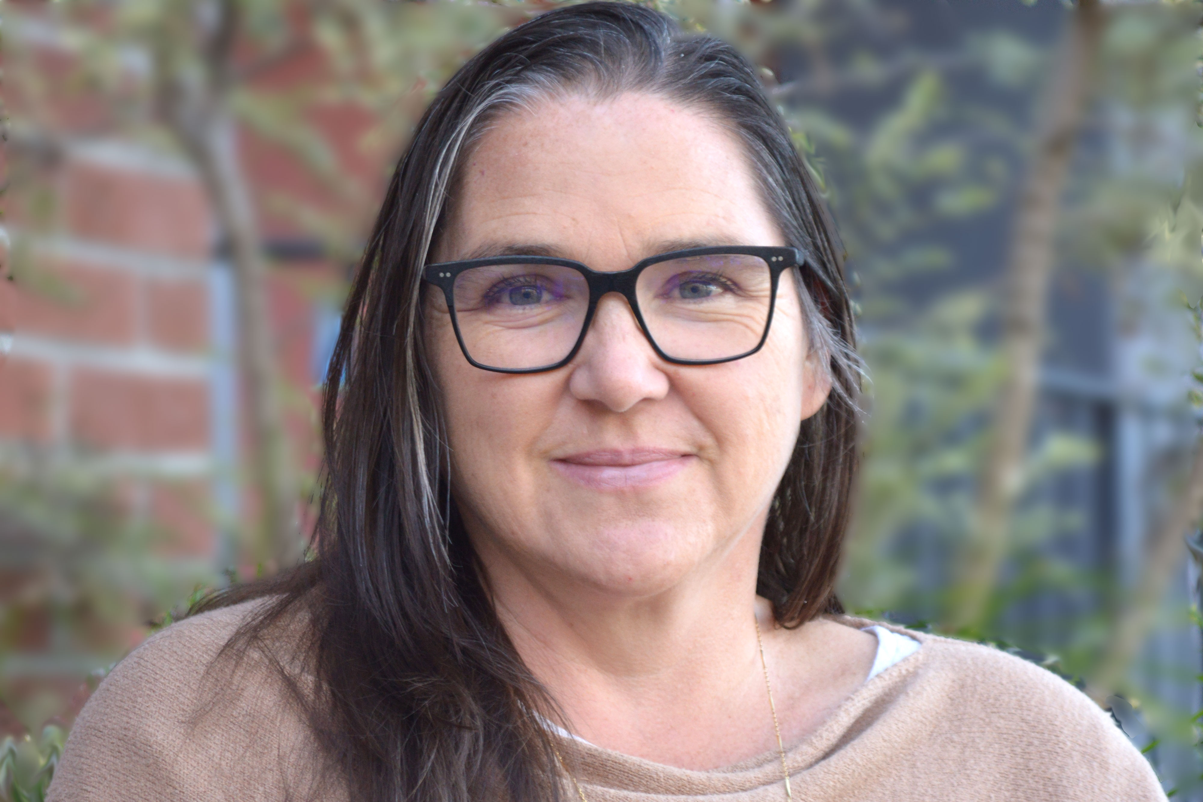 Sabina Brown — woman with dark hair and glasses in front of building and foliage
