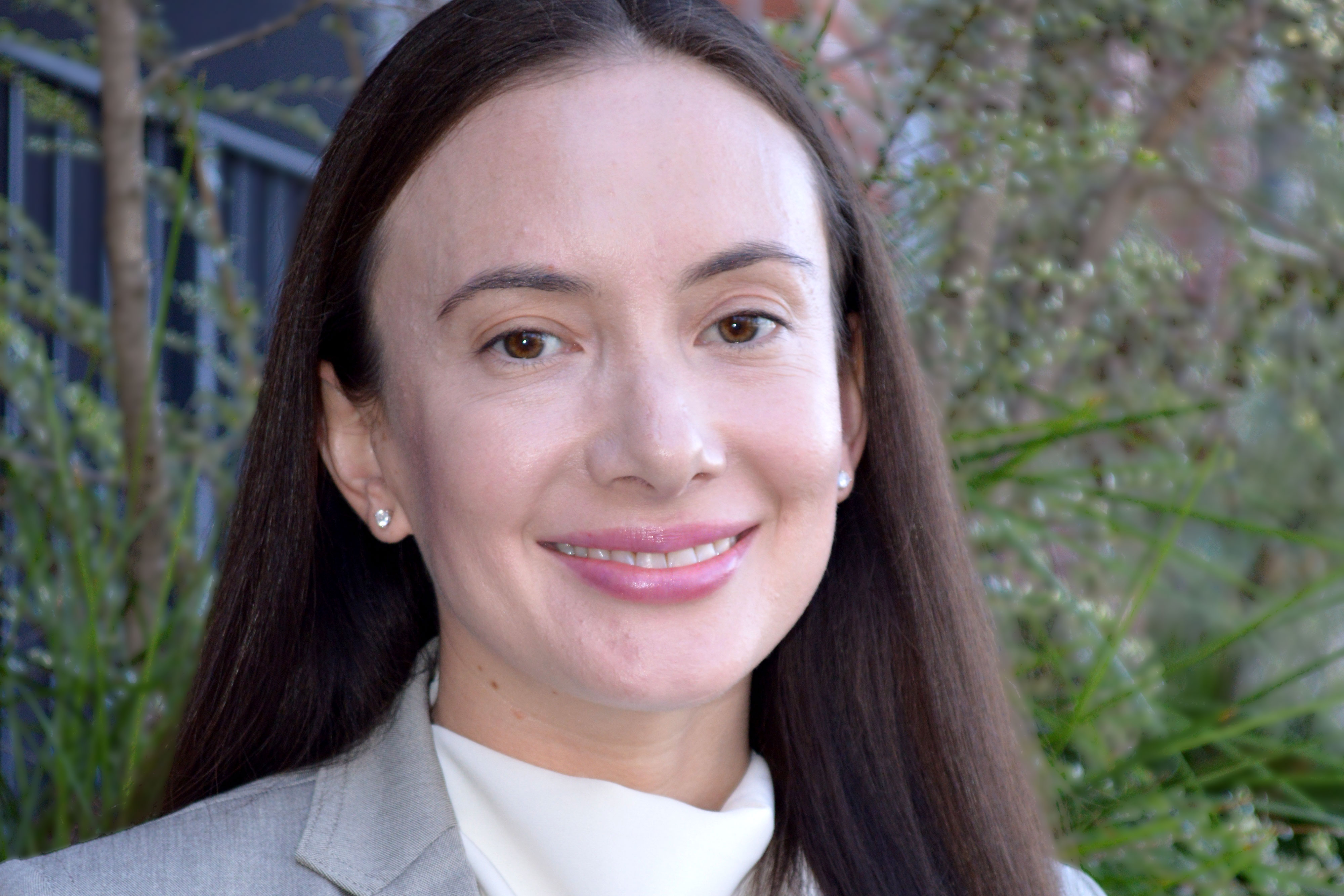 Leanna Reyes — woman with long dark hair, gray jacket and white blouse in front of foliage