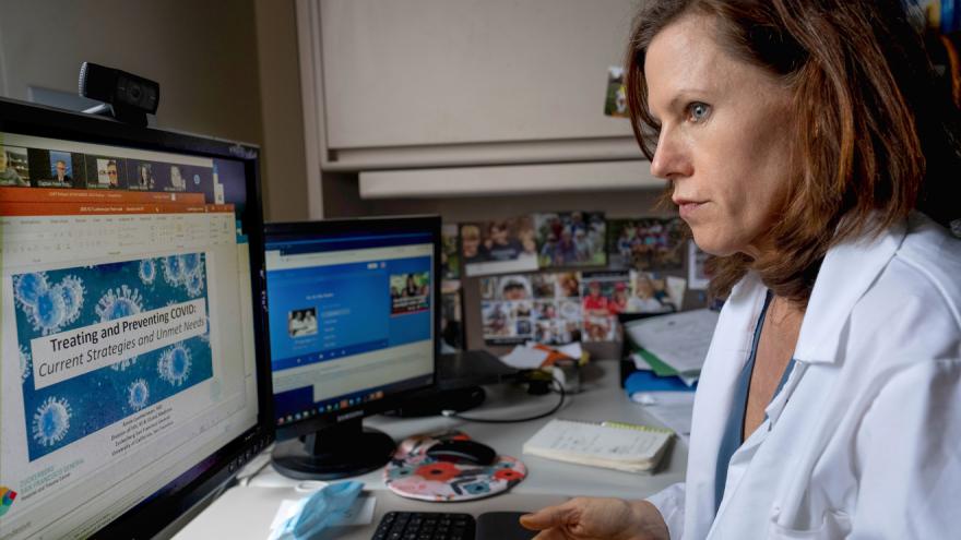 woman in white medical coat looks at computer screen