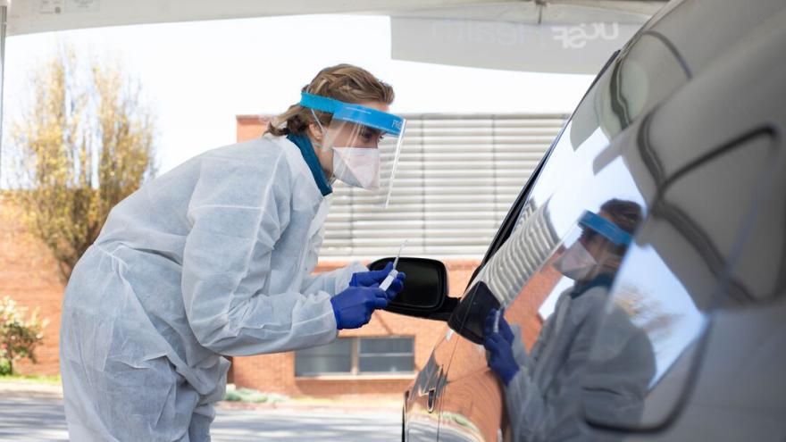 Person in PPE administering COVID test approaches a car at drive-in testing