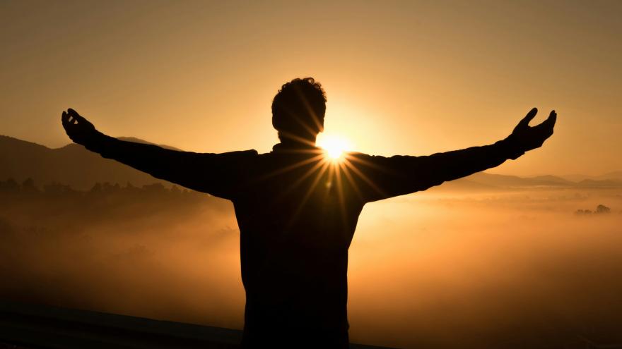 Silhouette of person opening arms with sun setting behind them