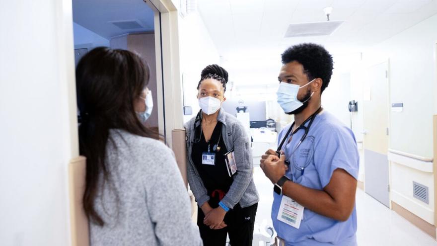 Two nurses wearing ID badges talking to another person