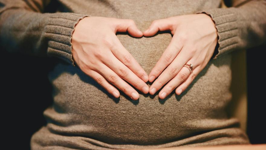 Pregnant person making a heart symbol with hands over belly