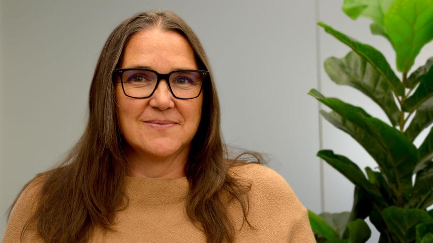 portrait of woman with long brown hair and glasses, next to plant