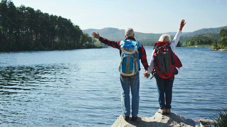 An older couple holds hands after completing a hike to a lake in the mountains