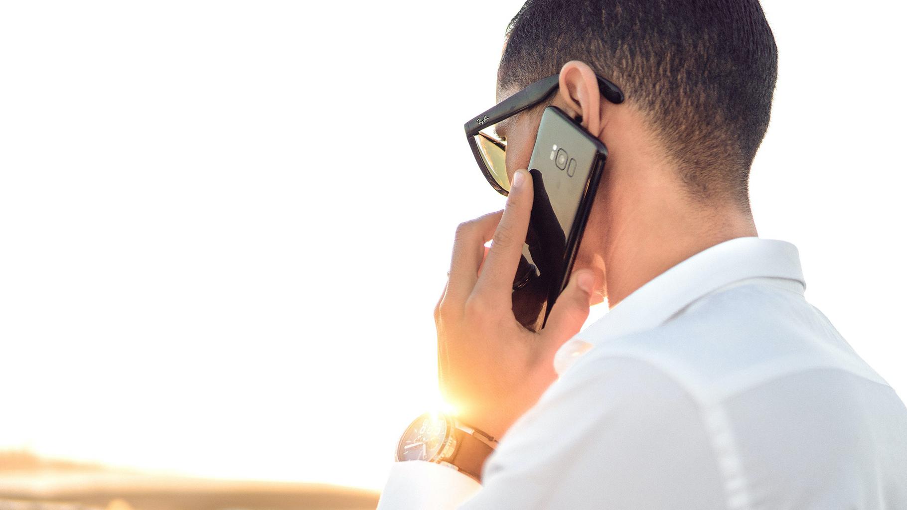 Person in white shirt talking on cell phone with head turned away