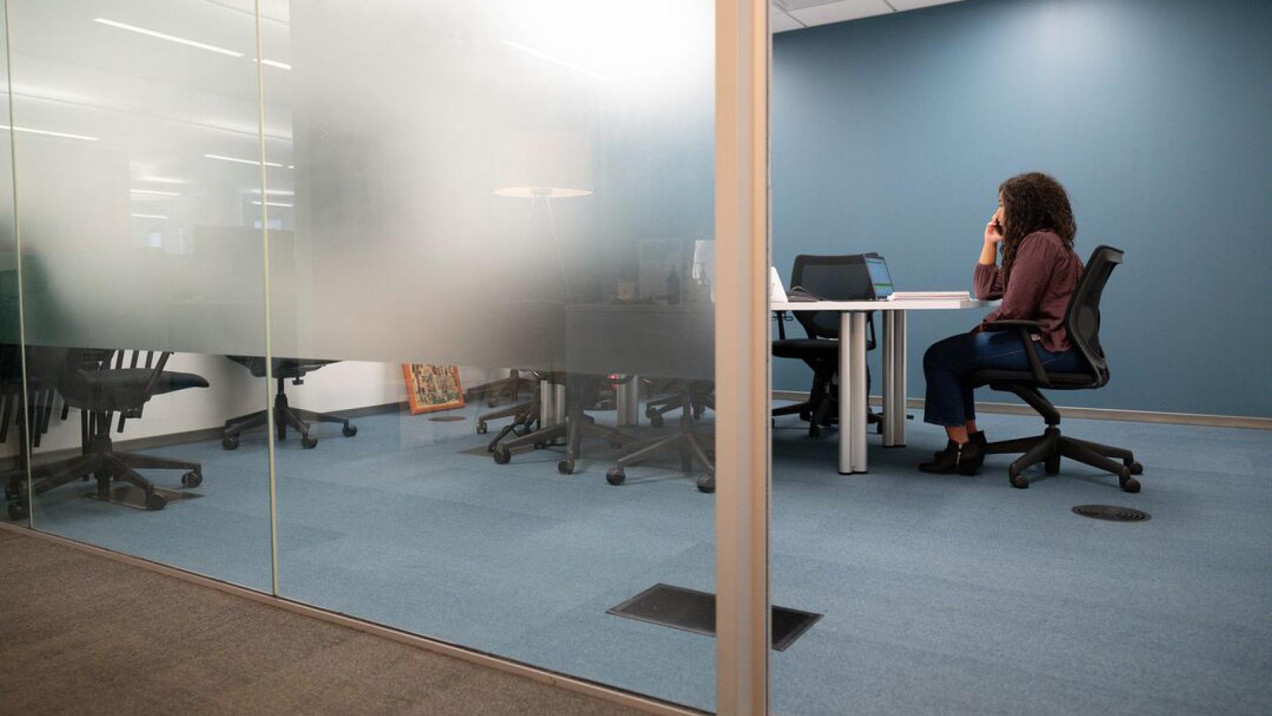 Person talks on phone and sits at laptop in conference room