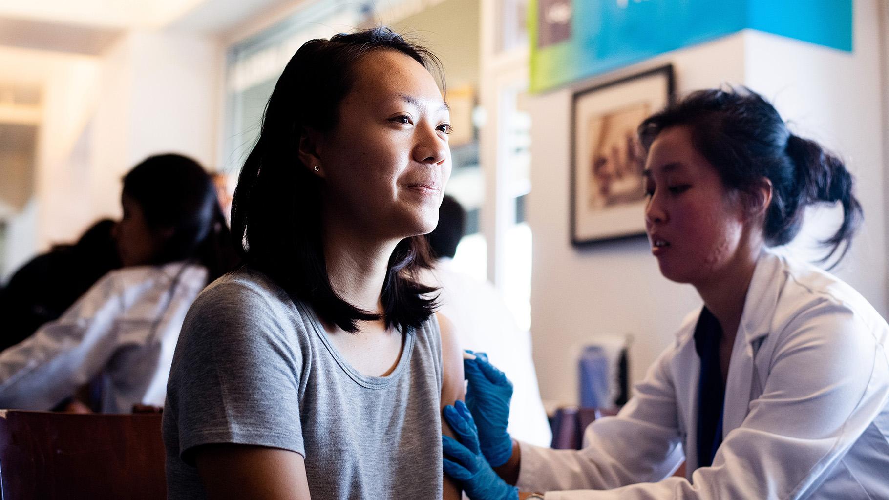 person sits for flu shot as nurse completes injection