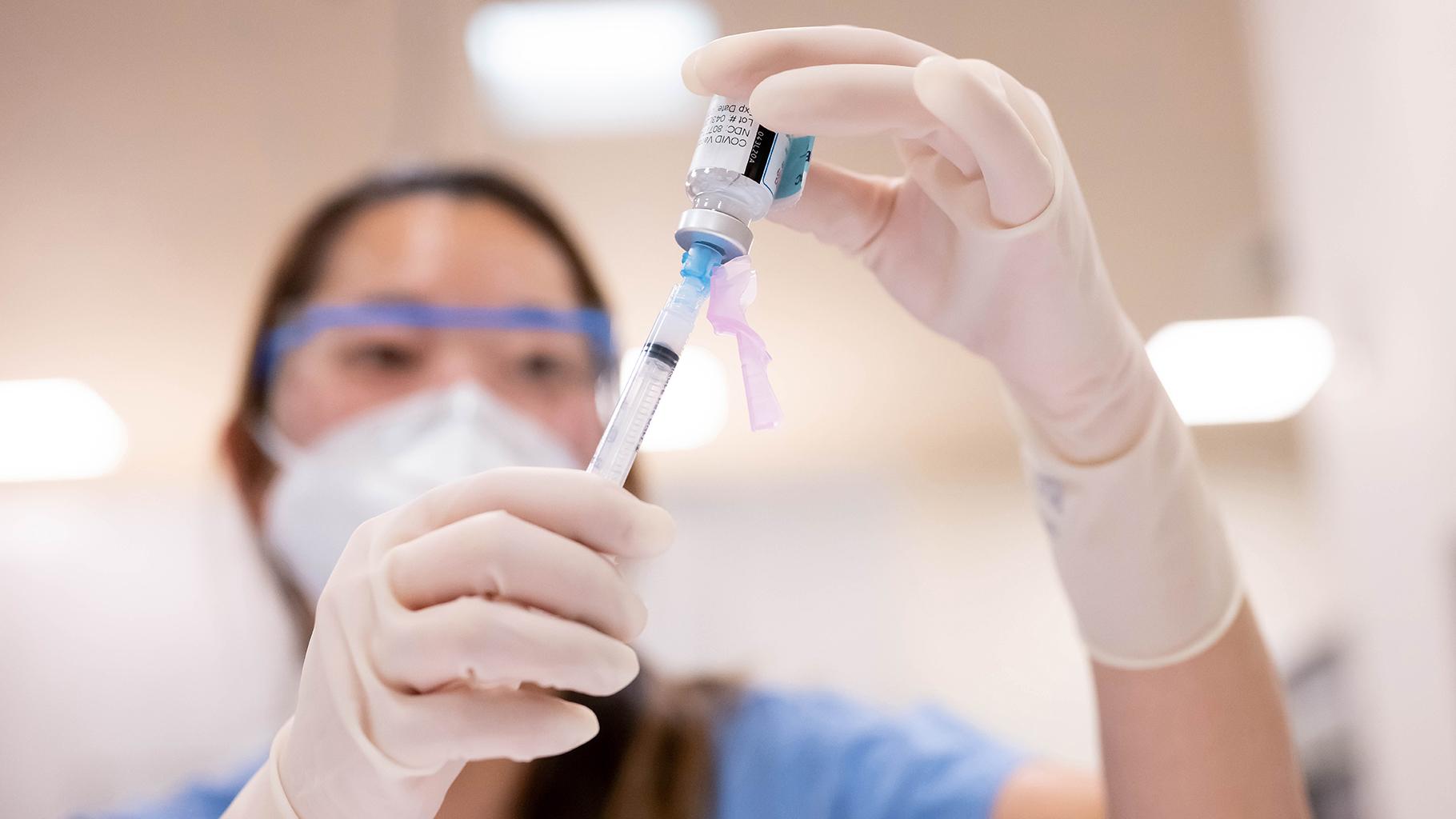 Nurse looks at syringe with COVID vaccine