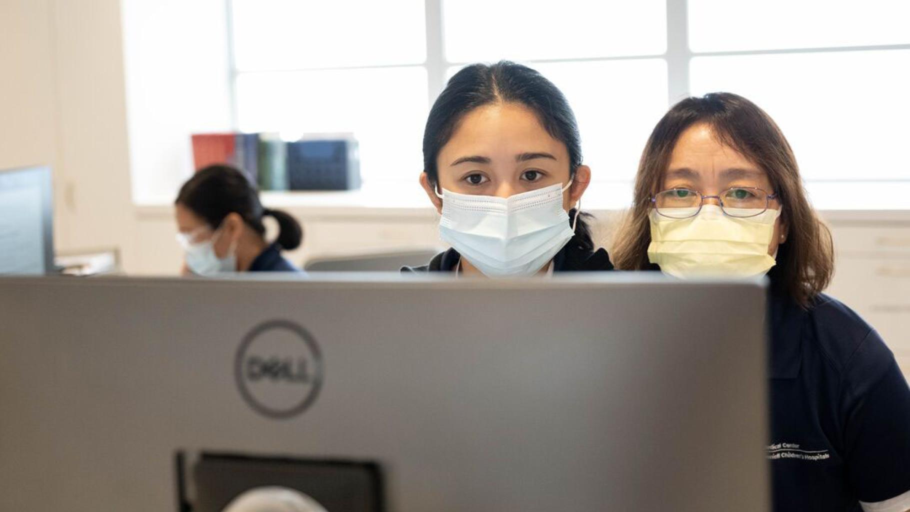 Two people in masks look at computer screen