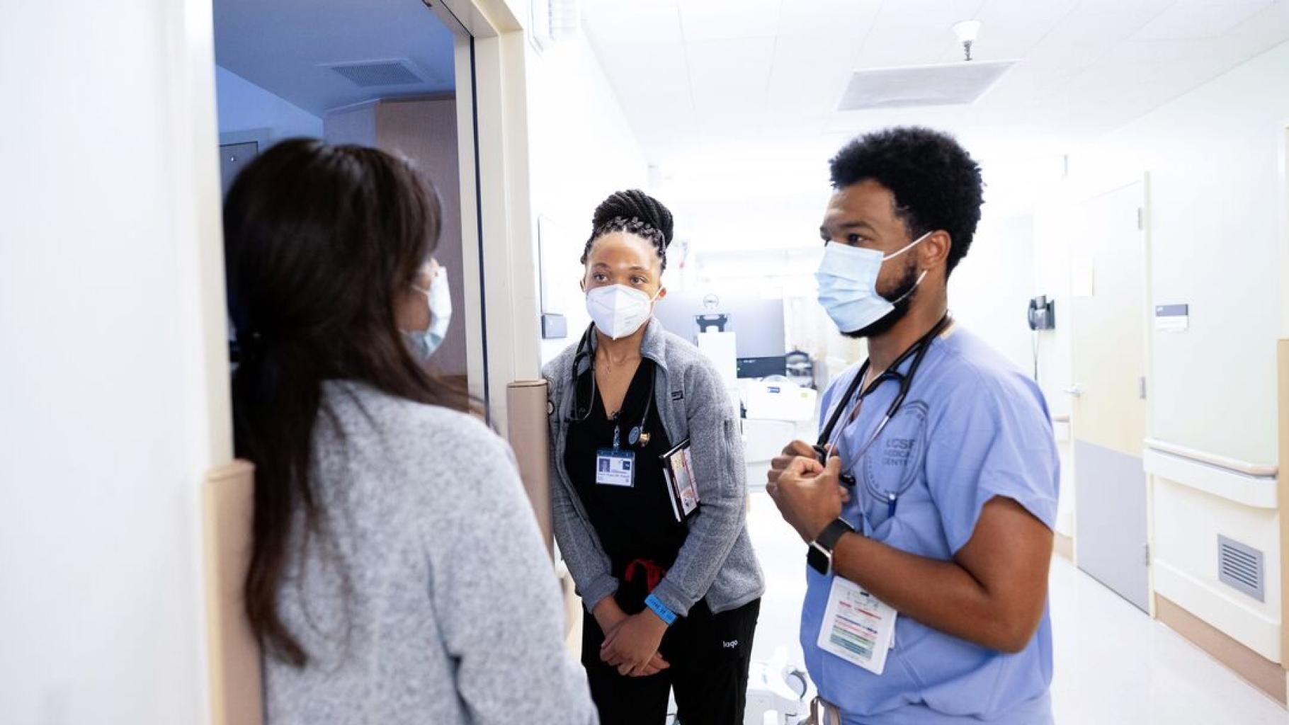 Two nurses wearing ID badges talking to another person