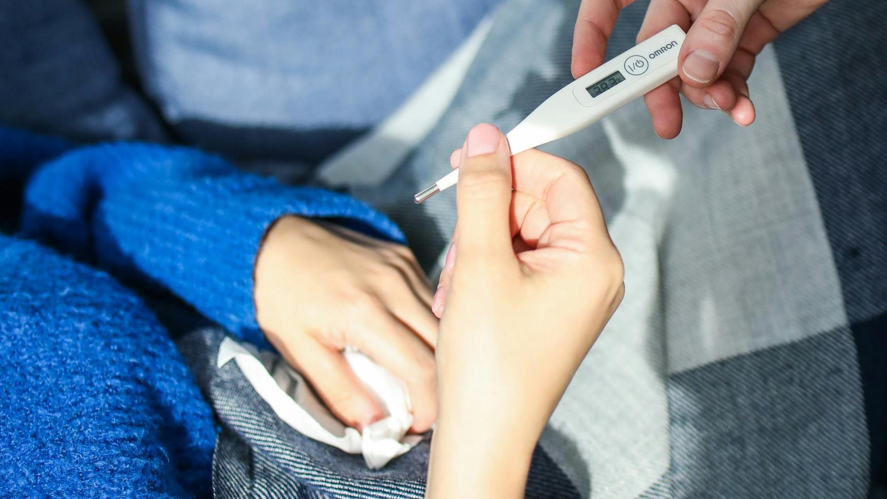 Sick person holding and looking at thermometer