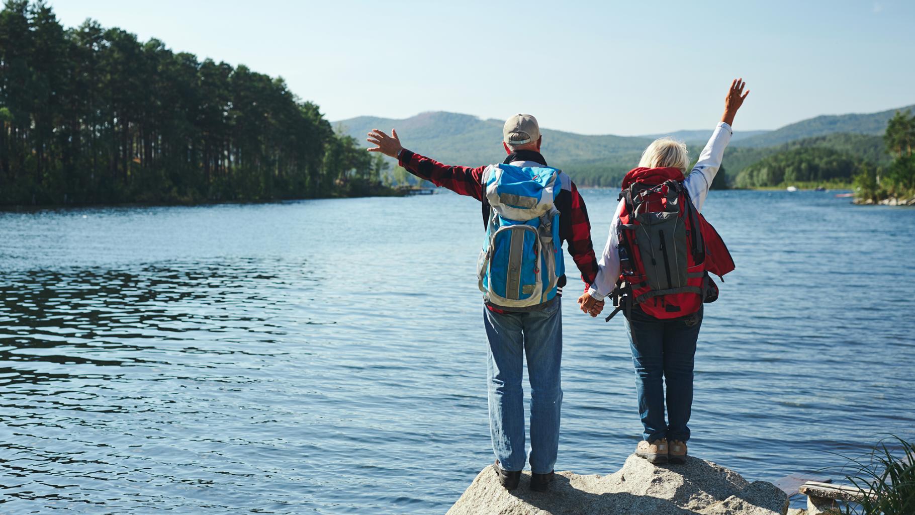 An older couple holds hands after completing a hike to a lake in the mountains